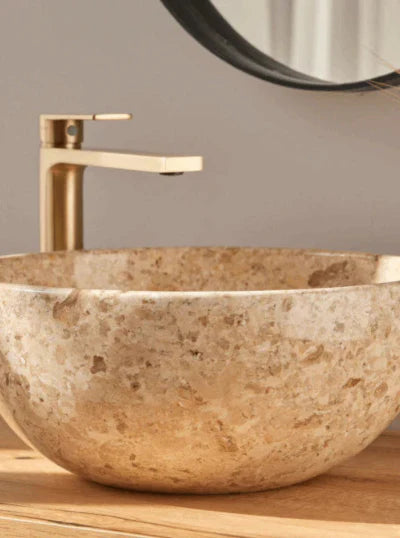 beige natuursteen waskom met gouden kraan