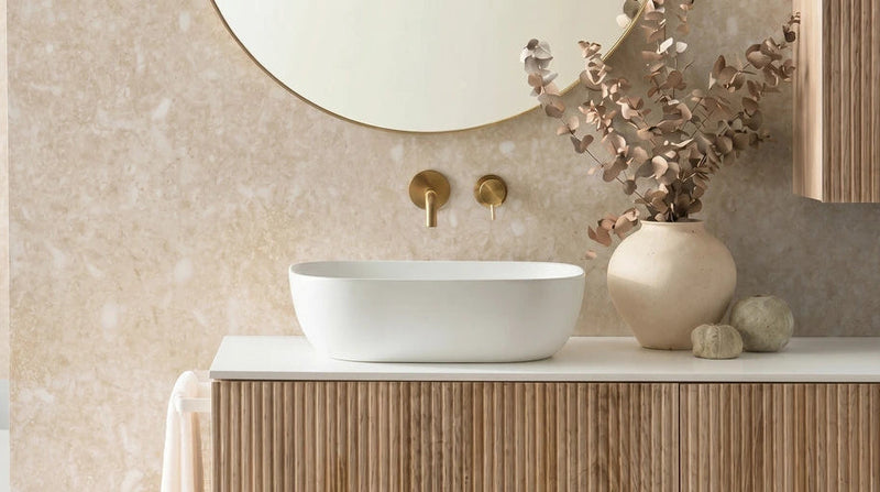 Witte ovale keramische waskom met gouden wandkraan op houten badmeubel met ribbelfront