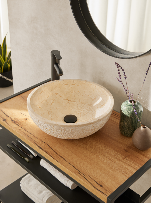 Ronde beige natuurstenen waskom 40x40x15cm met gepolijste binnenzijde en gehamerde buitenkant op houten badmeubel met zwarte opbouwkraan.