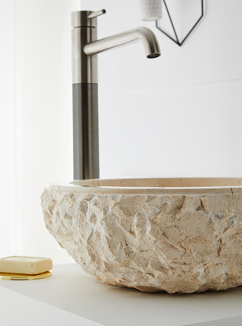 Ruw bewerkte natuursteen waskom in beige tint 50x50x25cm op strak wit blad, gecombineerd met geborsteld stalen kraan voor een natuurlijke uitstraling