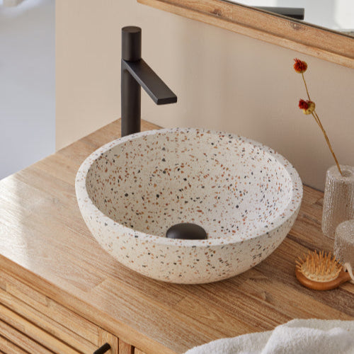 Terrazzo waskom in ronde vorm met kleurrijke chips op houten blad, gecombineerd met zwarte opbouwkraan en subtiele accessoires 35x35x12cm