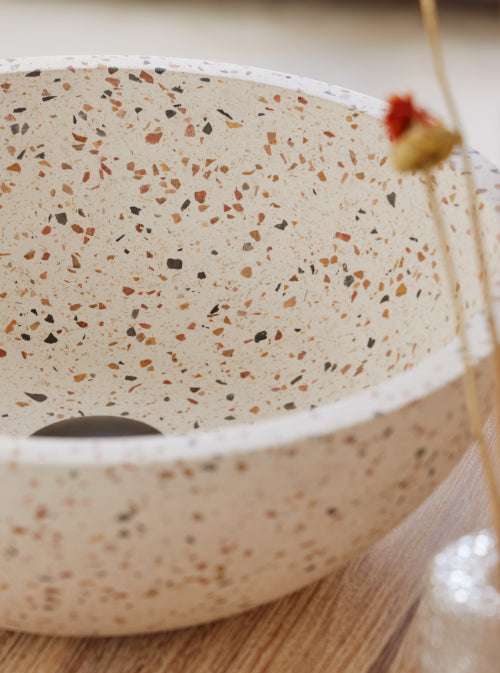 Ronde terrazzo waskom met multicolor steentjes op houten badmeubel met zwarte kraan en warme natuurlijke badkamerstyling 35x35x12cm