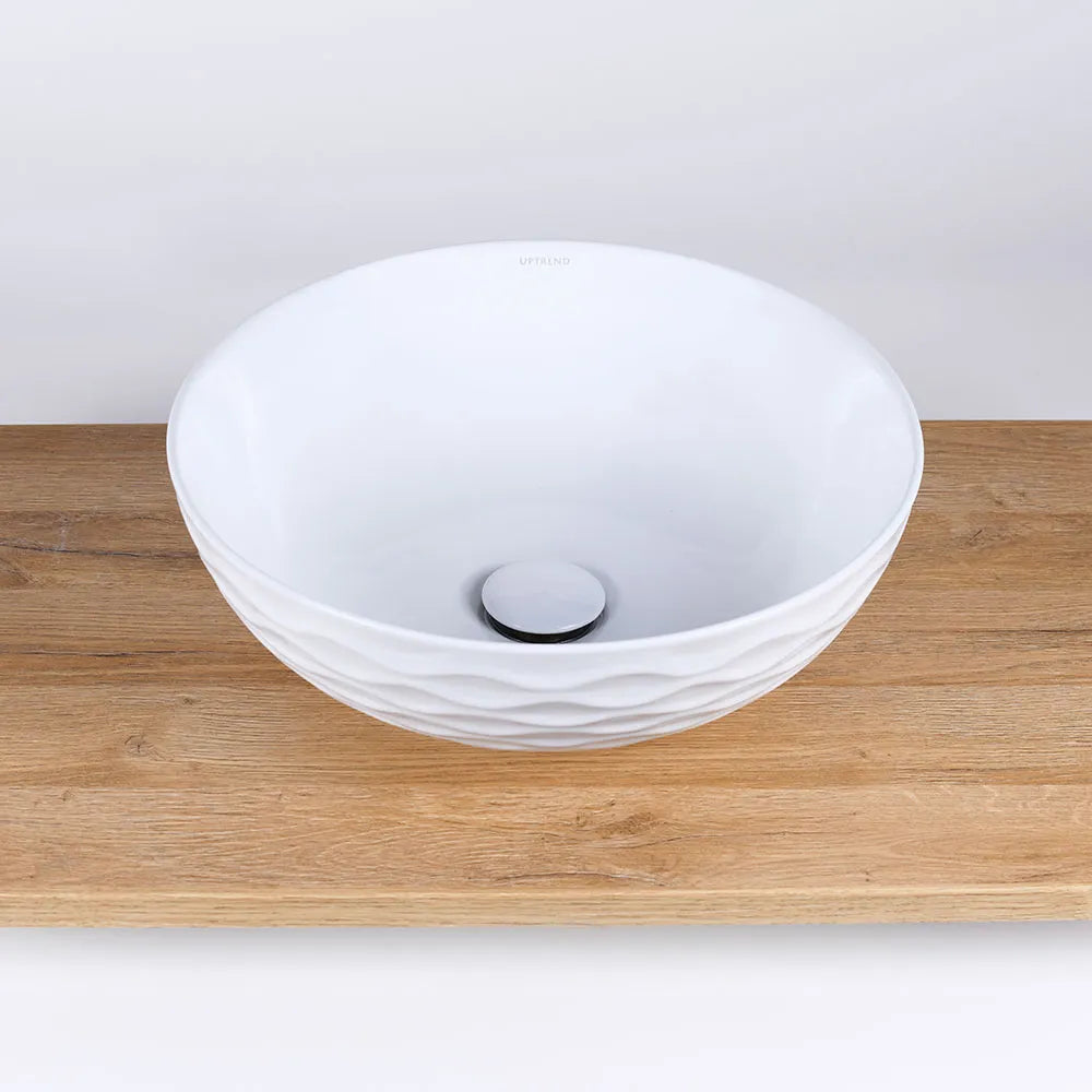 Ronde witte keramische waskom Arya met geometrisch reliëf op houten wastafelblad