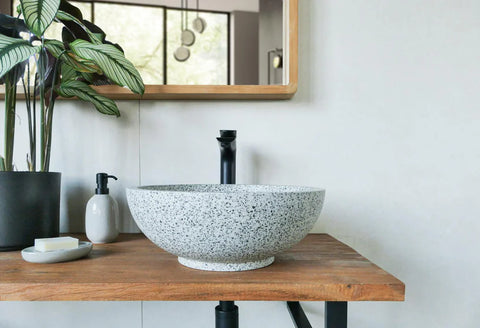 Ronde wit gespikkelde natuurstenen waskom terrazzo op houten blad met zwarte opbouwkraan in moderne badkamer