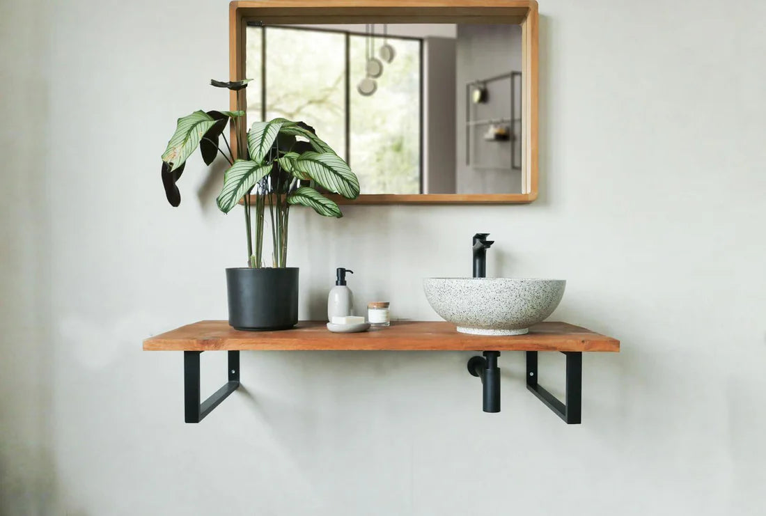 Witte, ronde, terrazzo natuurstenen waskom op houten wandplank met zwarte kraan en plant in moderne badkamer