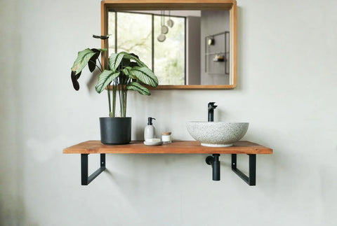 Witte, ronde, terrazzo natuurstenen waskom op houten wandplank met zwarte kraan en plant in moderne badkamer