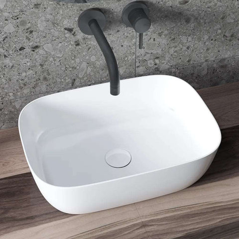 Witte rechthoekige keramische waskom op houten badmeubel met matzwarte wandkraan en grijze terrazzo wand in moderne badkamer.