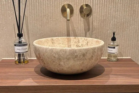 natuurstenen beige waskom voor een spatwand op een donker houten wastafelblad. 