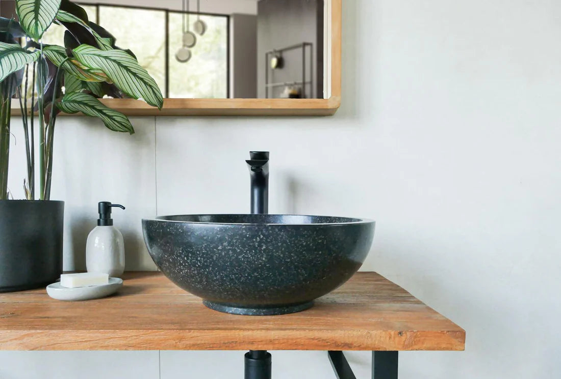 Ronde zwarte natuurstenen terrazzo waskom op houten blad met zwarte opbouwkraan in moderne badkamer