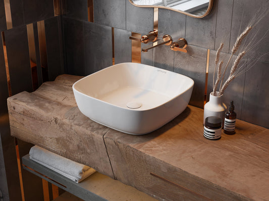 Vierkante witte waskom van keramiek geplaatst op een stoer houten badmeubel met koperen wandkraan