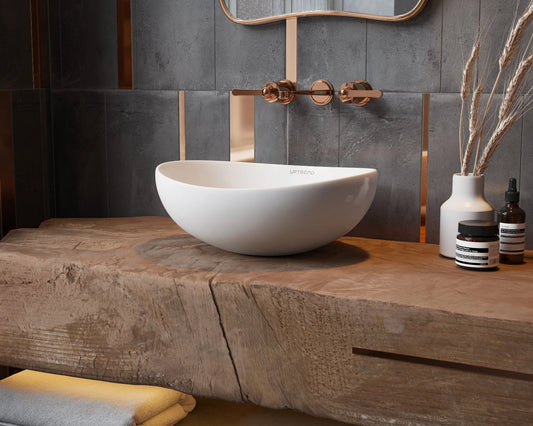 Witte ovale opzetwaskom op massief houten wastafelblad met koperen wandkraan